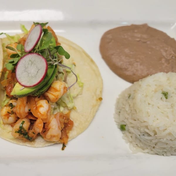 Shrimp tacos with avocado, radish, and microgreens, served with rice and refried beans.