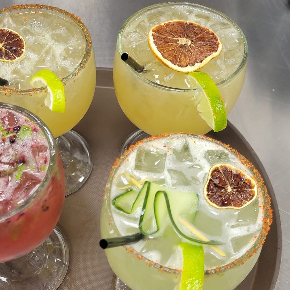 Four Mr. Sombrero margaritas on a tray, two with dried orange, one with lime, and one with cucumber.