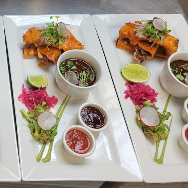 Two plates of Mr. Sombrero's Mexican birria tacos with various sauces, guacamole, and pickled onions.