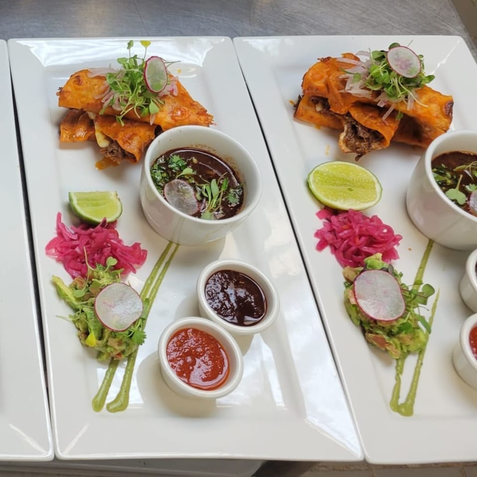 Two plates of Mr. Sombrero's Mexican birria tacos with various sauces, guacamole, and pickled onions.