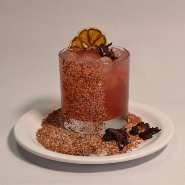 A Mr. Sombrero cocktail, garnished with a dried orange slice and hibiscus, on a plate with chili salt.
