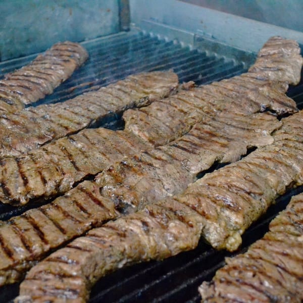 Marinated skirt steak, known as arrachera, sizzling on a grill with visible grill marks.