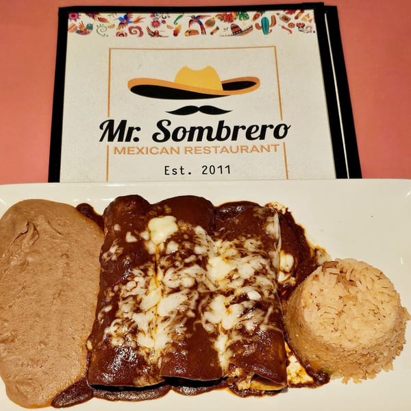 Mr. Sombrero enchiladas with mole sauce, melted cheese, refried beans, and rice on a white plate.