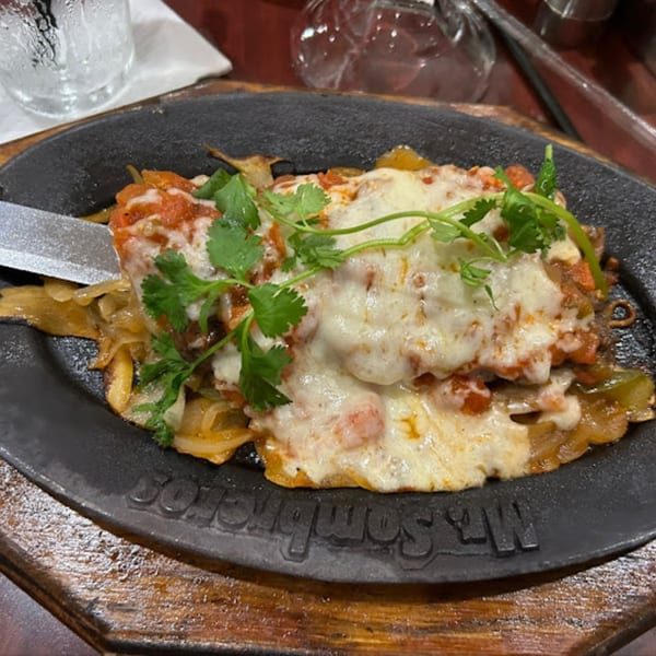 Mr. Sombrero's sizzling Mexican dish with melted cheese, onions, peppers, and cilantro on a cast iron platter.