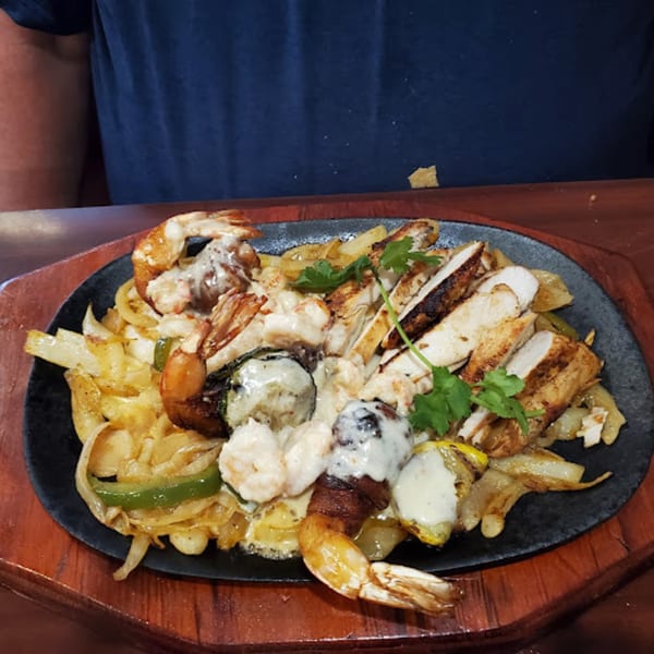 Sizzling Mr. Sombrero fajitas with chicken, shrimp, onions, and peppers on a black platter.